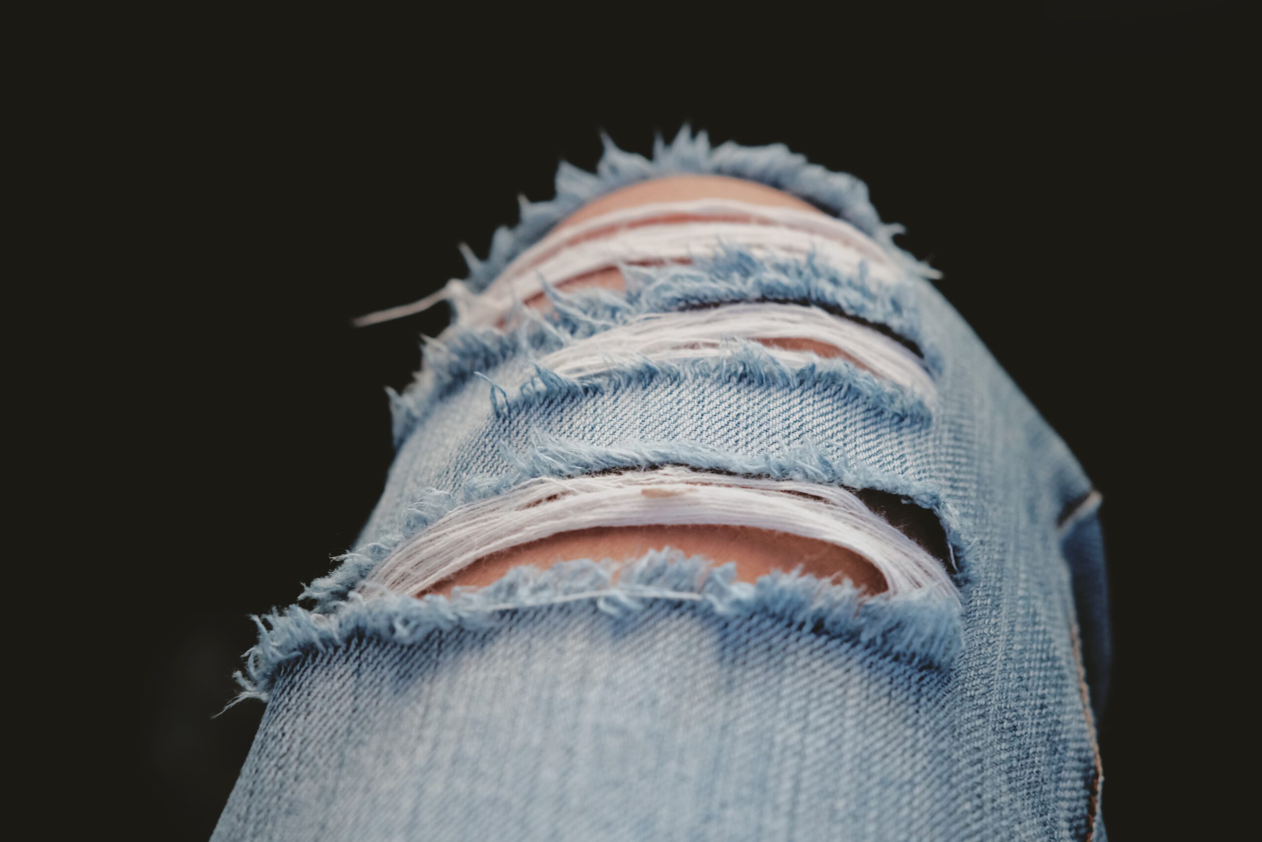 Dziura w jeansach na kolanie postrzępiona wokół na ciemnym tle